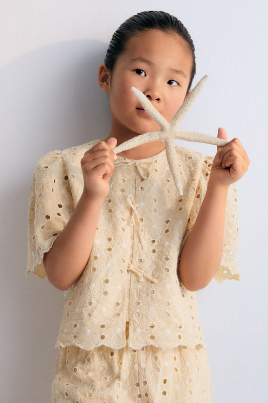 Creta Blouse in embroidered blend cotton fabric in macadamia color, featuring gathered sleeves, a high neckline, and central bow closure. New Collection Kids