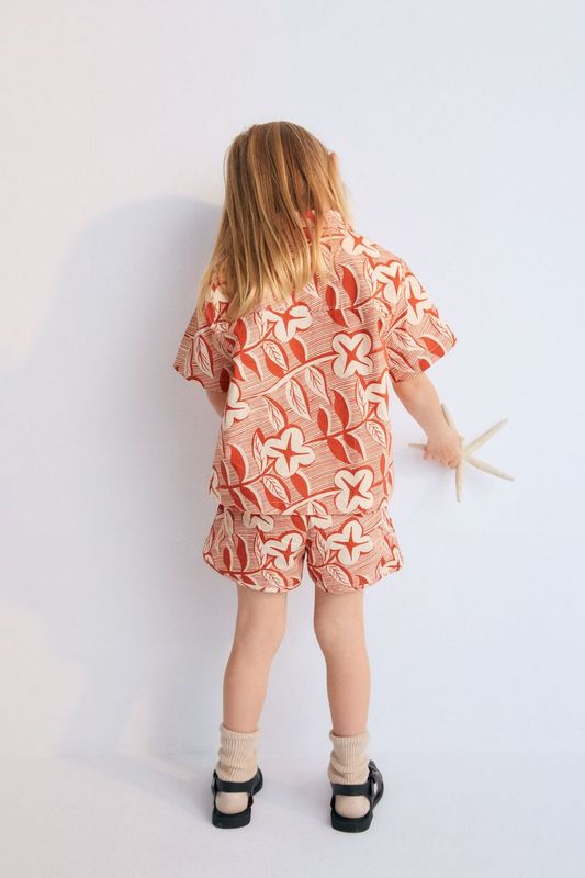Filotis Short in 100% cotton fabric with our chili mountain rose print, featuring an elastic waistband in chili with macadamia-colored letters. Spring Summer Collection. The New Society. 