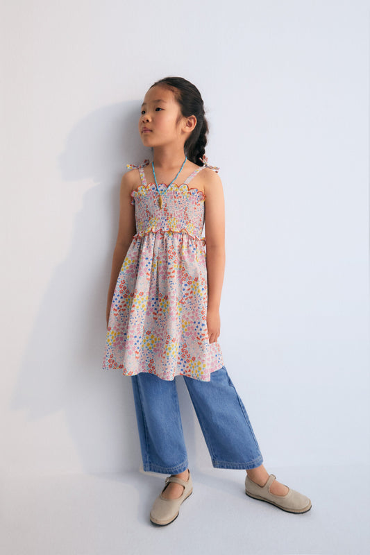 Greneva Dress in 100% cotton voile fabric with our anemone print. Dress with bow straps, smocking, and final ruffle with embroidery in our chili color. Skirt with ruffle and embroidery detail in chili. Spring Summer Collection. The New Society.